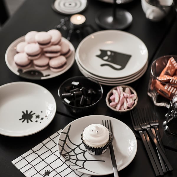 Several KUSTFYR side plates with Halloween-themed decor are placed on a black table along with treats and decorations.
