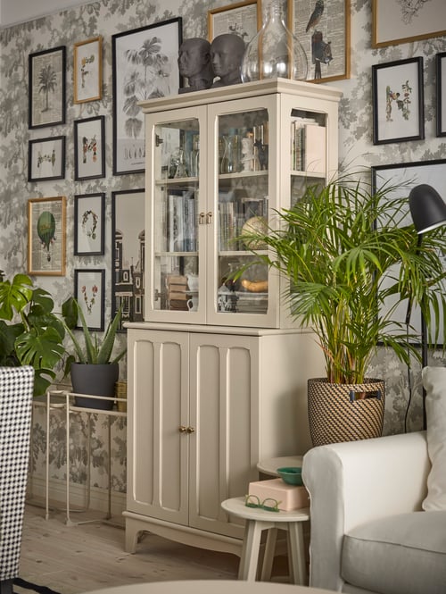 Dining area with a cabinet with glass doors, a potted plant, a plant stand, a round table, and multiple framed pictures.