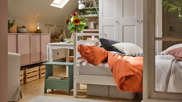 A rustic-style bedroom contains a white HAUGA extendable table next to a white TARVA bed with red-brown ÄNGSLILJA bed linen.