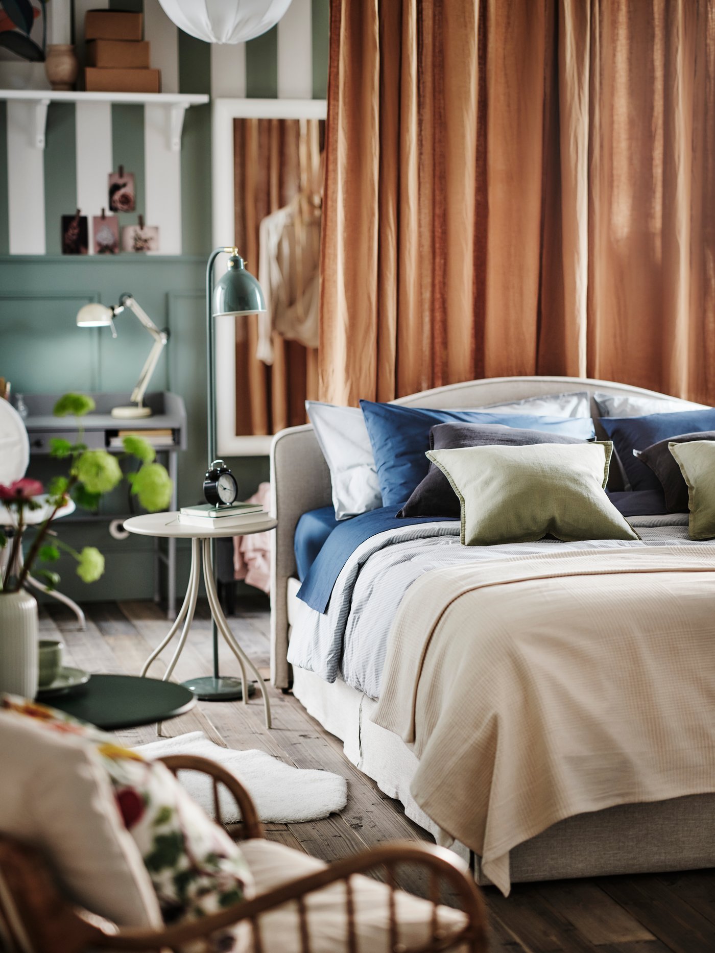 A beige RAMNEFJÄLL upholstered bed with a blue/striped BERGPALM comforter on it along with a mix of cushions and a bedspread.