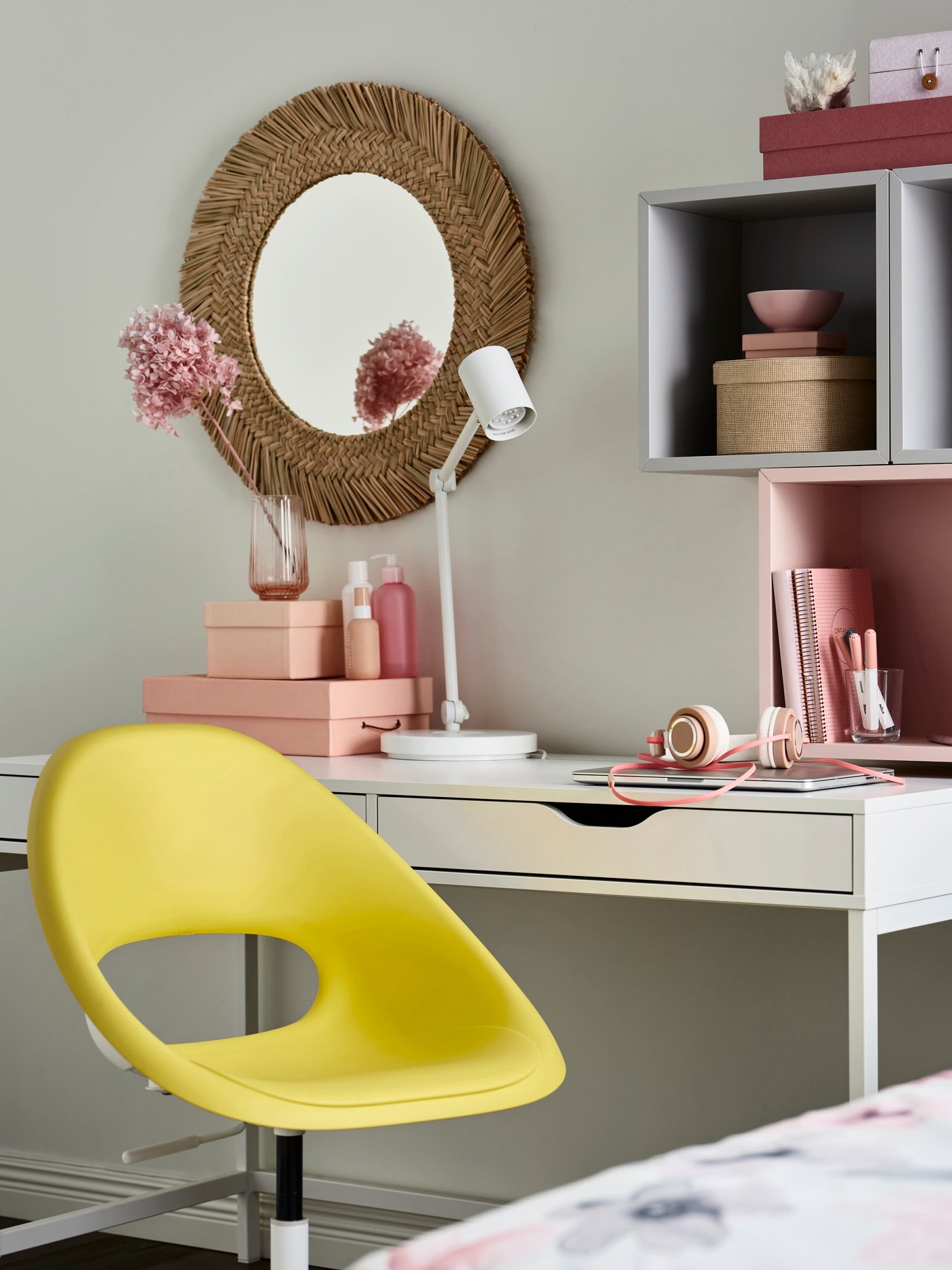An IKEA ELDBERGET office chair in bright yellow in front of an ALEX white desk with drawers, pink boxes and wall units and a rattan round mirror on the wall.