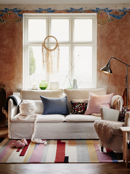 A living room with a standard three-seat sofa with multiple cushions, a floor reading lamp, and a throw on a wing chair.