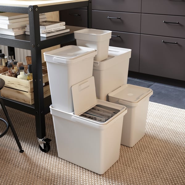 The image shows a white trash bin filled with several empty metal cans. Some cans have labels removed, and one can has a visible pull tab on the lid. This image could be relevant or interesting in discussions about recycling, waste management, or environmental issues.