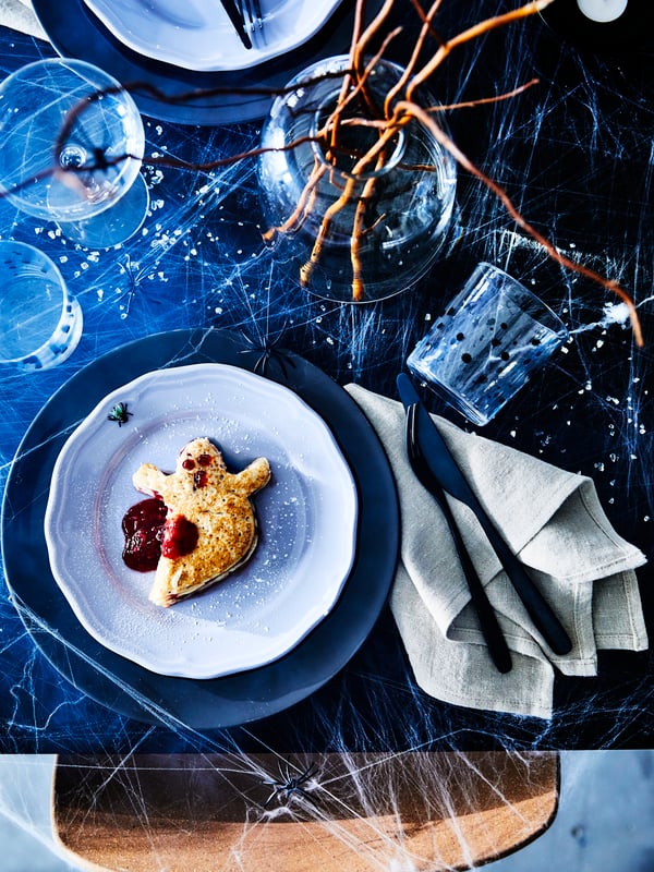 Dark plates on a table setting with spider webs and a ghost-shaped cookie. 