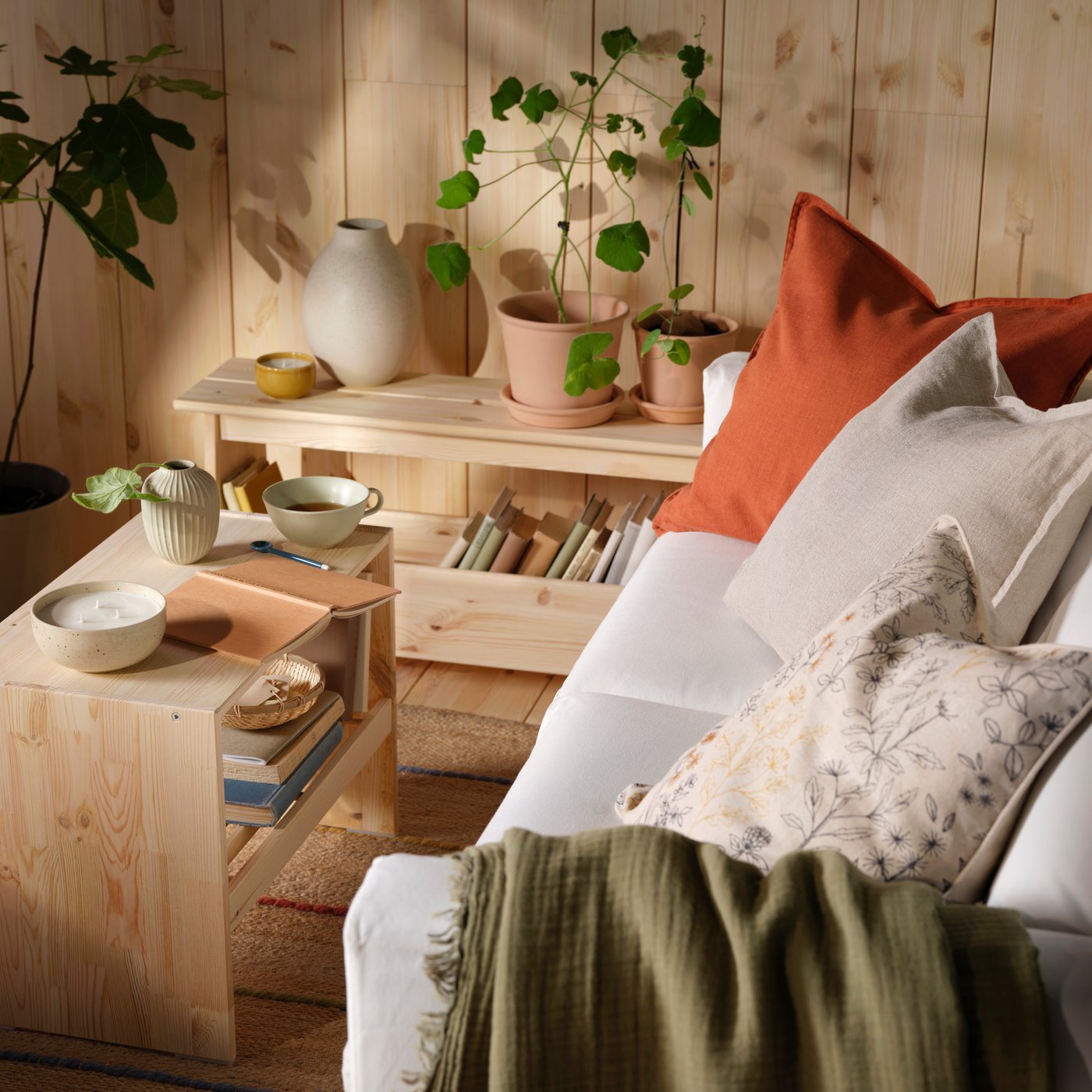 A beige sofa with DYTÅG cushion covers and a green VALLKRASSING throw, by a wooden coffee table with books and plants.