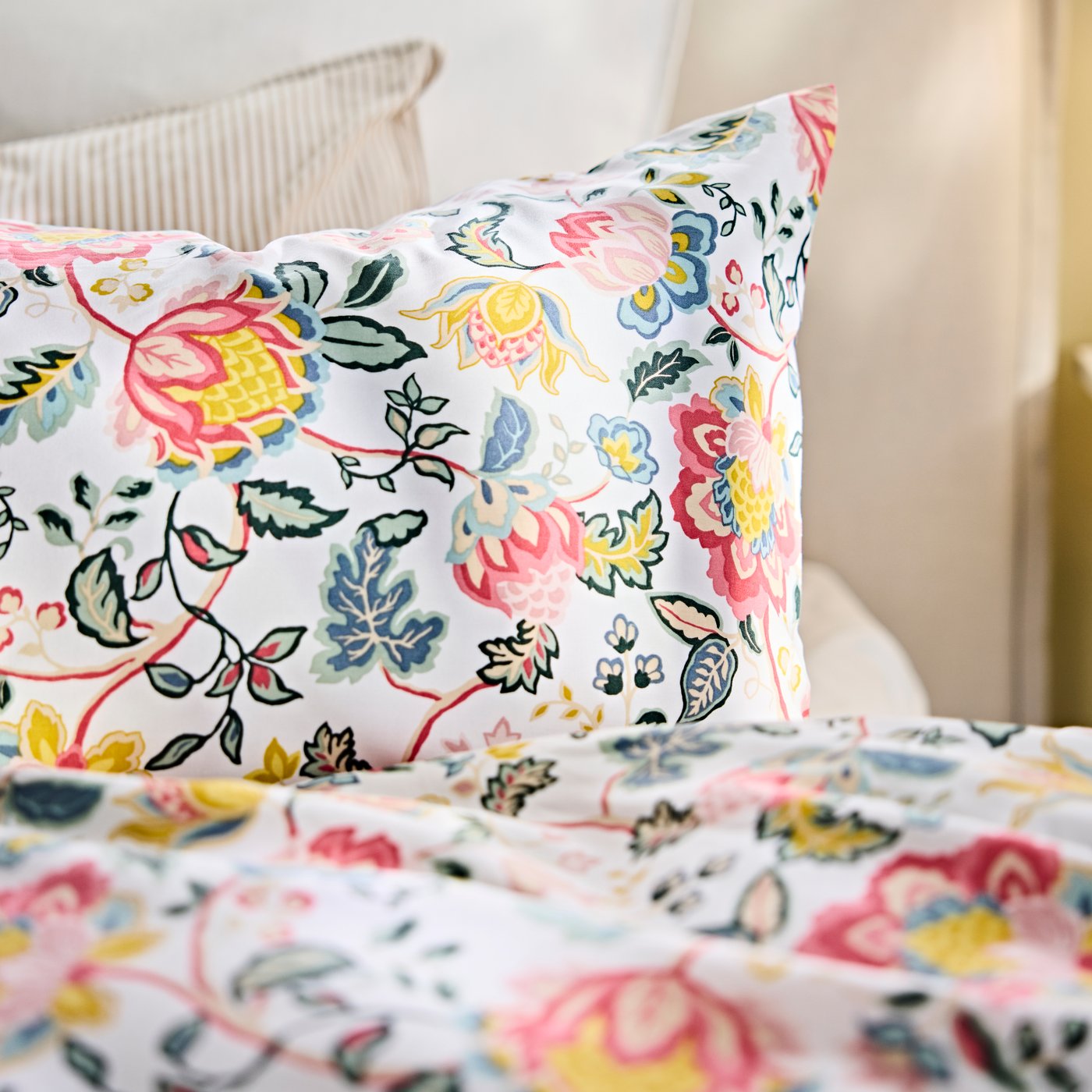 DAGSSALVIA pillow case with a floral pattern placed on a bed in a light bedroom setting with neutral cushions behind.