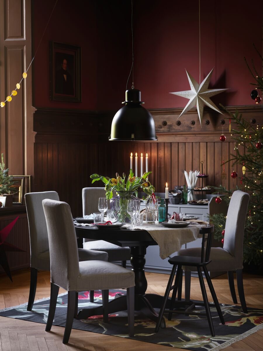 A festive holiday table is set with a round black dining table and grey dining chairs around it, with a black ceiling lamp above.