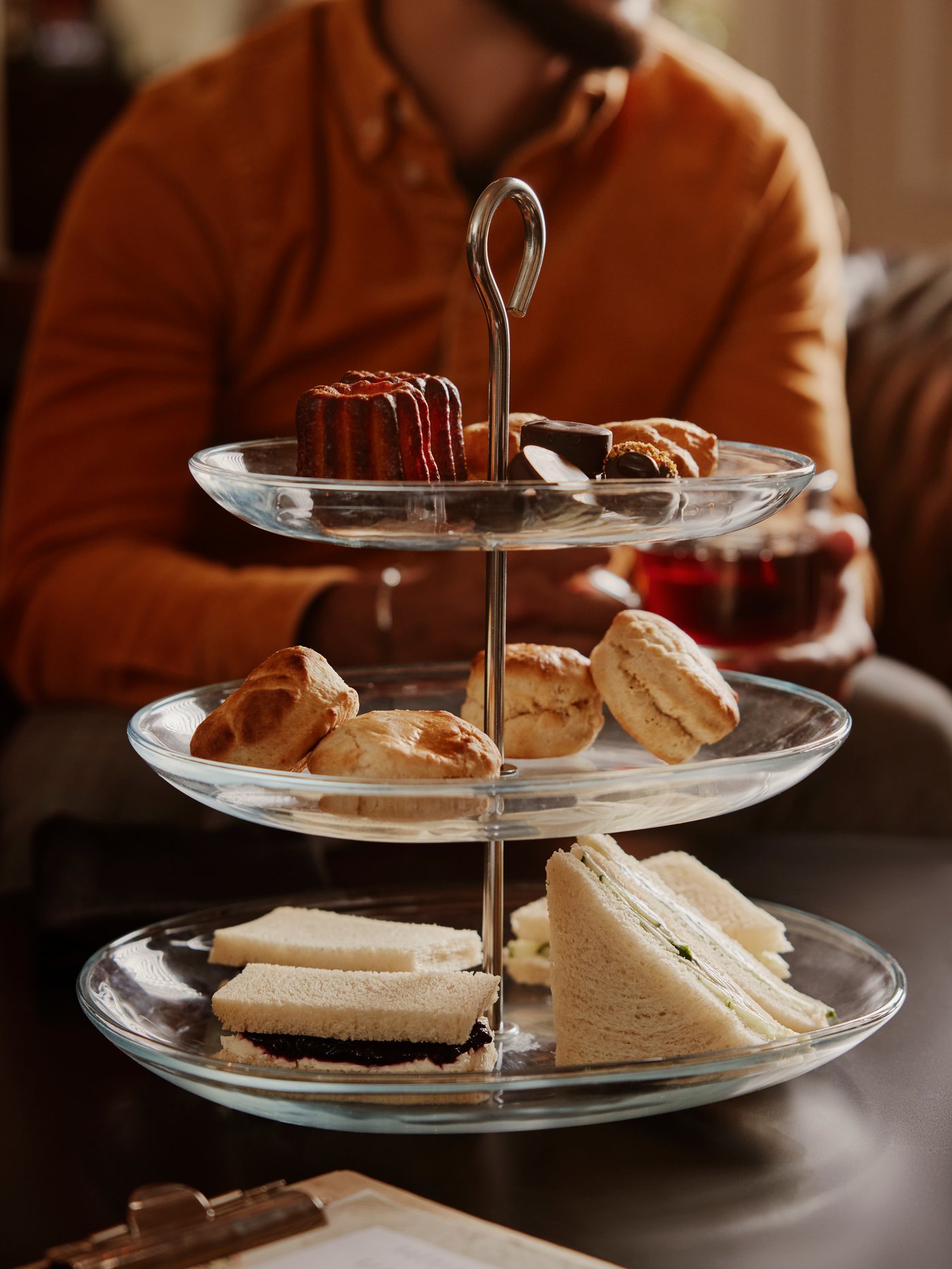 Fuente para servir de vidrio de tres pisos con comida panes y pasteles en cada uno de sus pisos.
