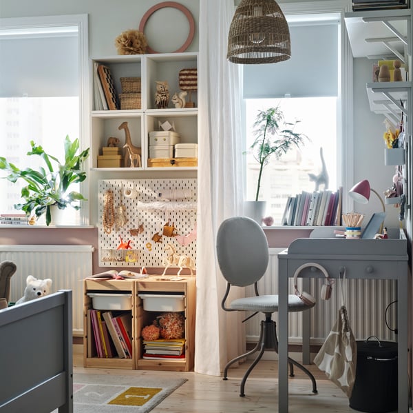 A cosy children’s bedroom with a grey SMYGA desk beside a window with a white curtain and a SKÅDIS pegboard behind it.