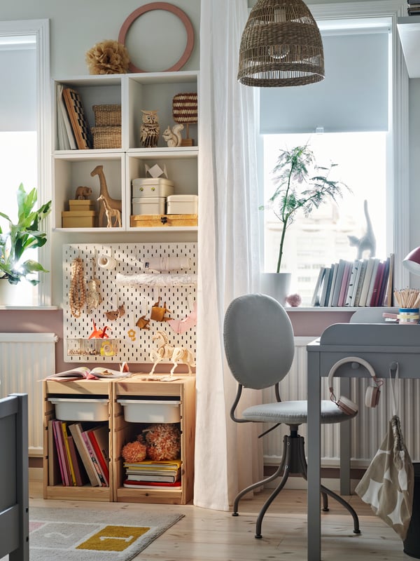 A cosy children’s bedroom with a grey SMYGA desk beside a window with a white curtain and a SKÅDIS pegboard behind it.