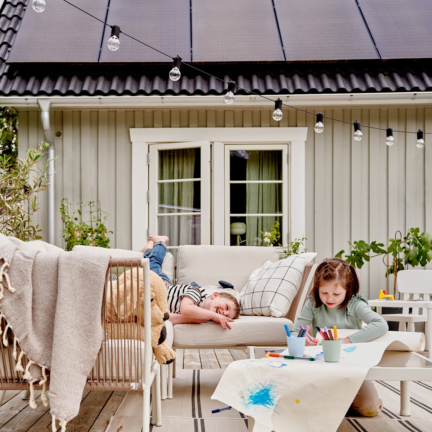 Side of a cottage with kids on outdoor furniture in front.