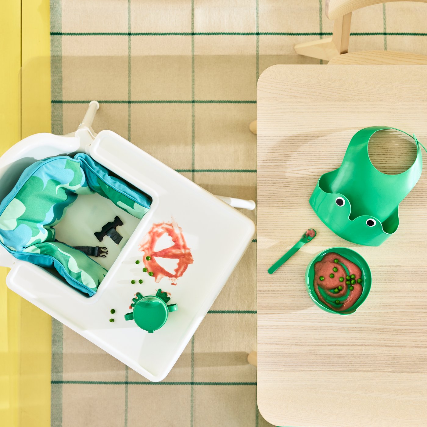 An ANTILOP highchair in white, by a table that has diverse items on it and beside other chairs for adult family members.