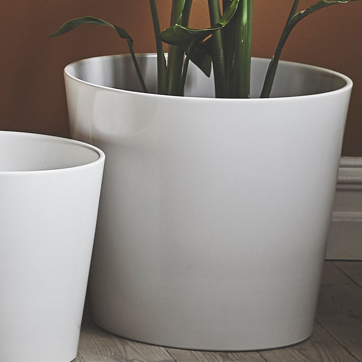 Två stora vita krukor stående på golv. 