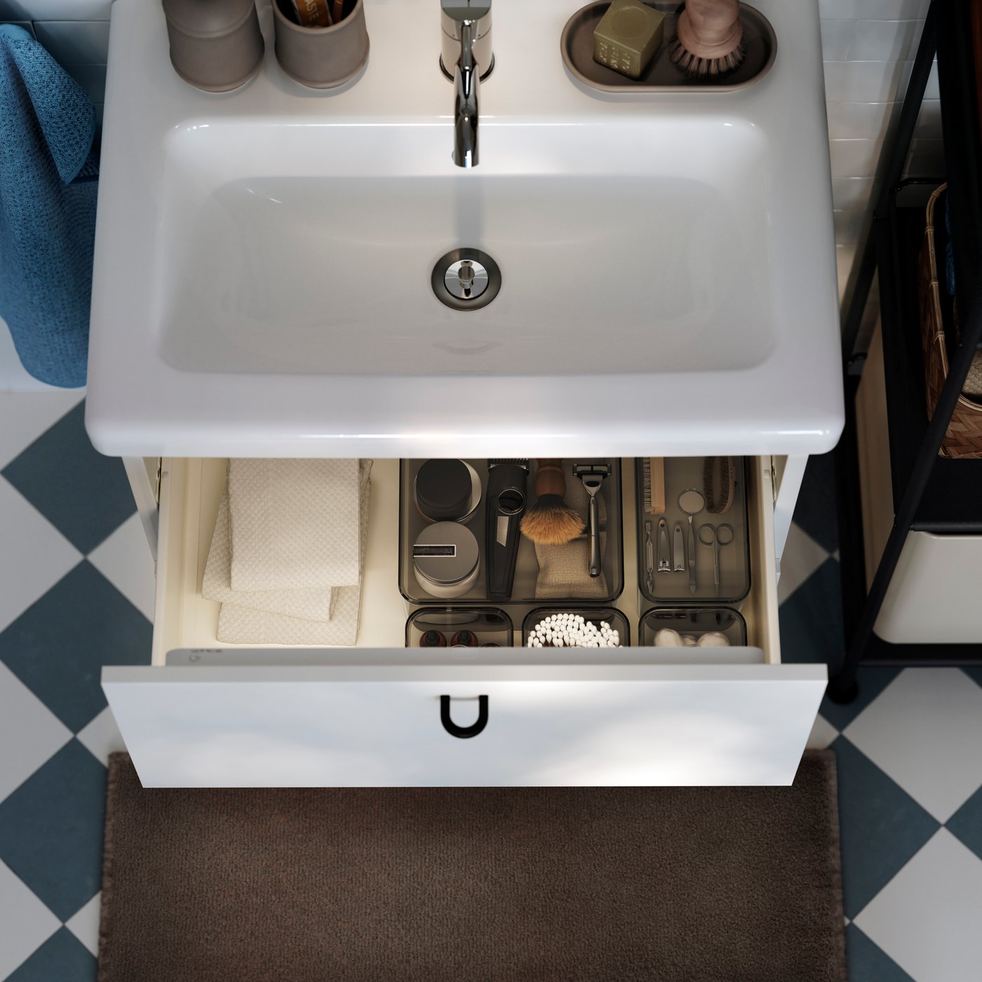 Vista dall'alto di un mobile per lavabo ENHET/TVÄLLEN bianco. Il cassetto superiore è aperto e mostra alcuni contenitori in cui sono organizzati prodotti per radersi.
