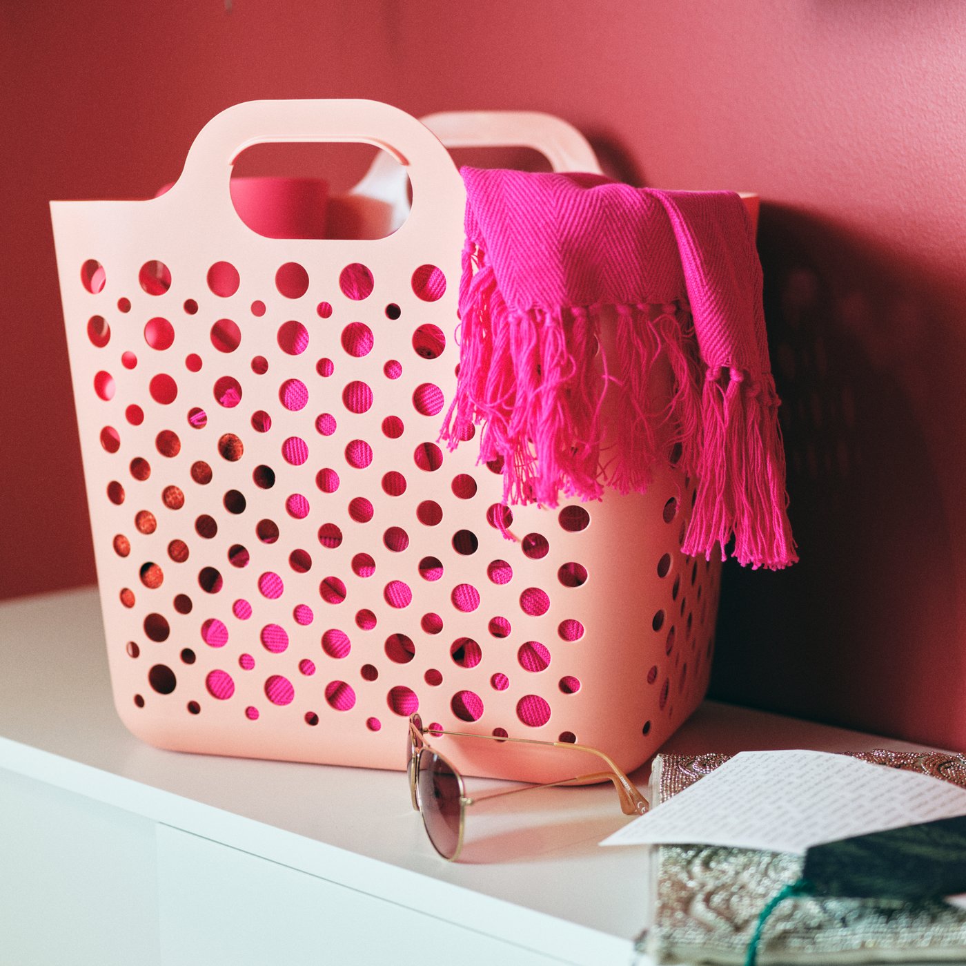 A pink SLIBB flexible laundry basket holding accessories standing on a white MACKAPÄR bench with storage compartments.