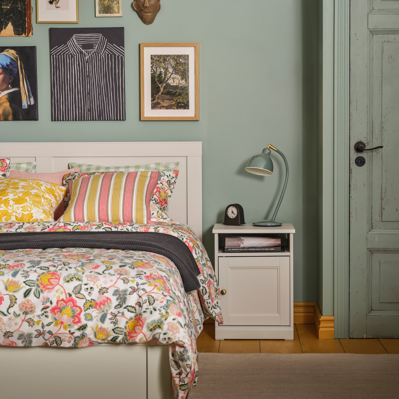 A bedroom with an off-white FÅGELFJÄLLET bed frame with 4 storage boxes, neatly arranged with colourful bedding and art.