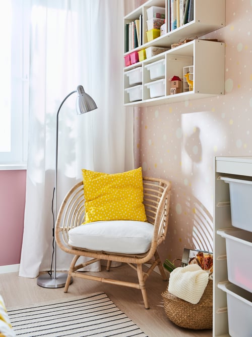 Living room with white and pink walls, with an armchair with yellow cushion next to a floor lamp, and a wall storage above.