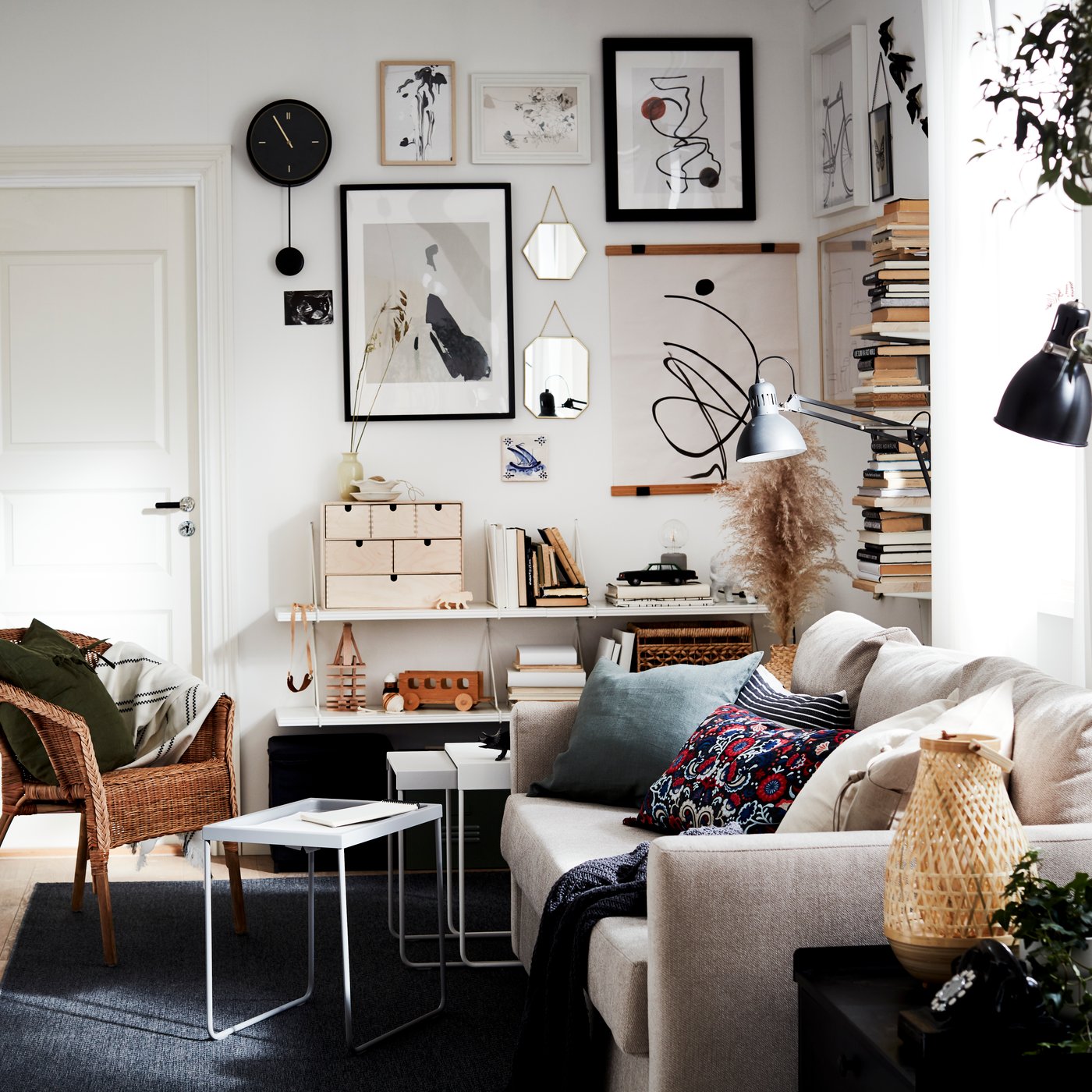 A small living room area with lots of light, a sofa, a TV, a vertical book display and an art wall, all in neutral colours.