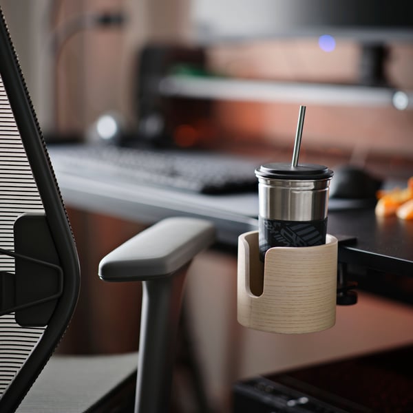 A LÅNESPELARE mug holder in ash veneer is fastened to a black UTESPELARE gaming desk. A STYRSPEL gaming chair is at the desk.