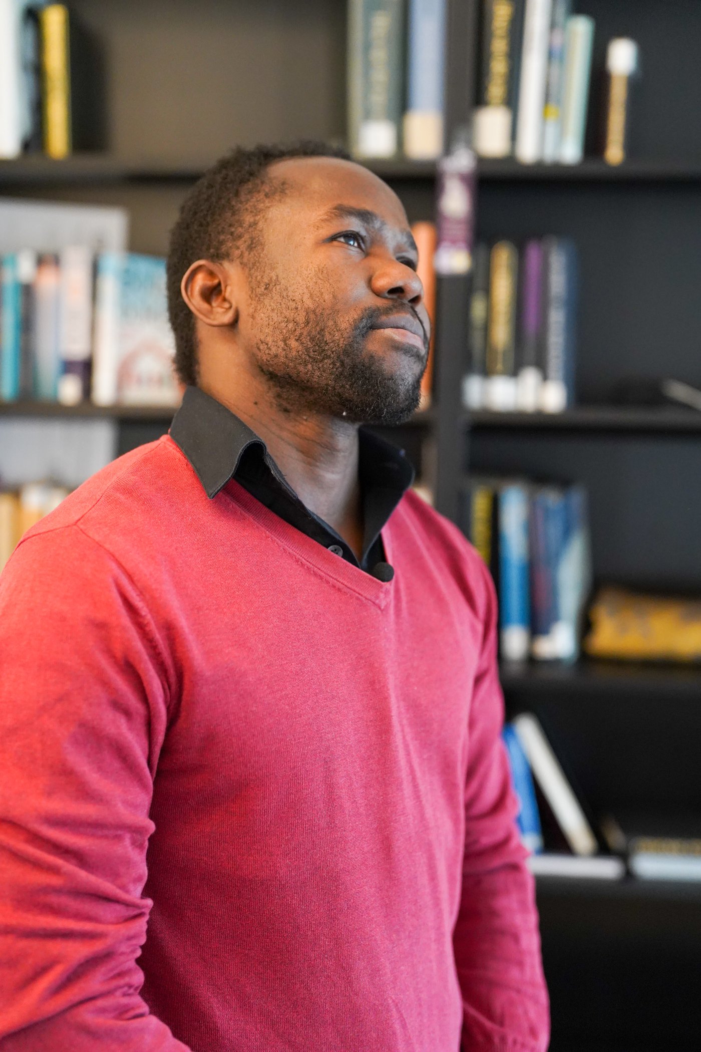 A man standing inside a livingroom in a red shirt looking up at the ceiling. 