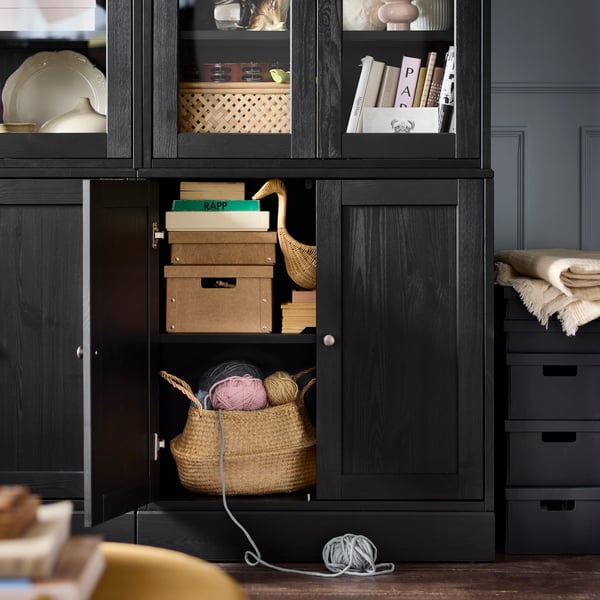 A black HAVSTA storage combination with one cabinet door open, revealing stacked boxes and a basket of knitting accessories.