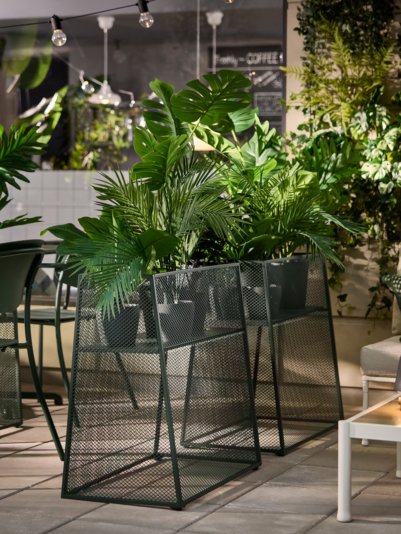 Deep green VISINGSÖ plant stands with green plants in a modern café setting with outdoor seating.