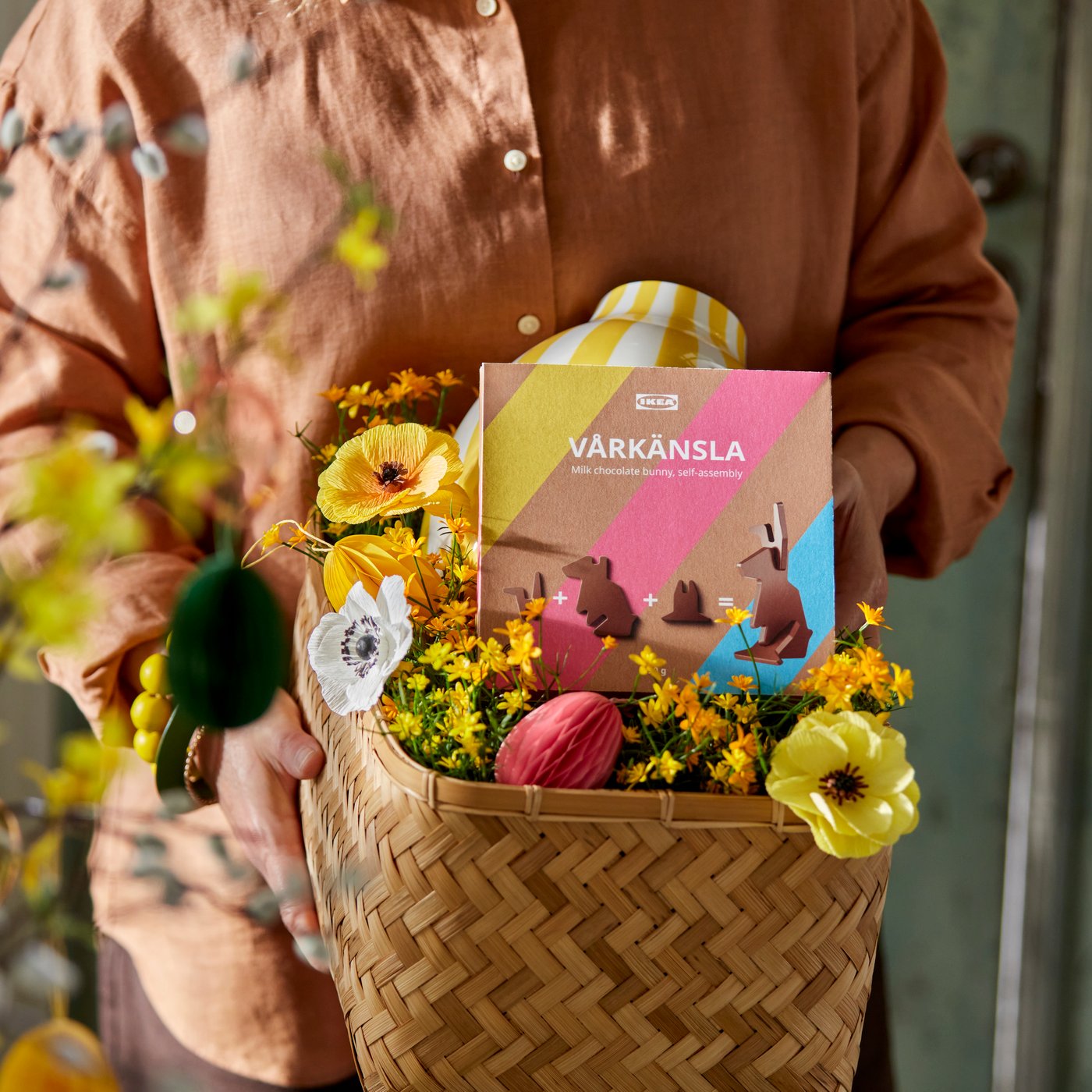 EN eprson holder en kurv fyldt med kunstige blomster og en chokolade påskekanin 