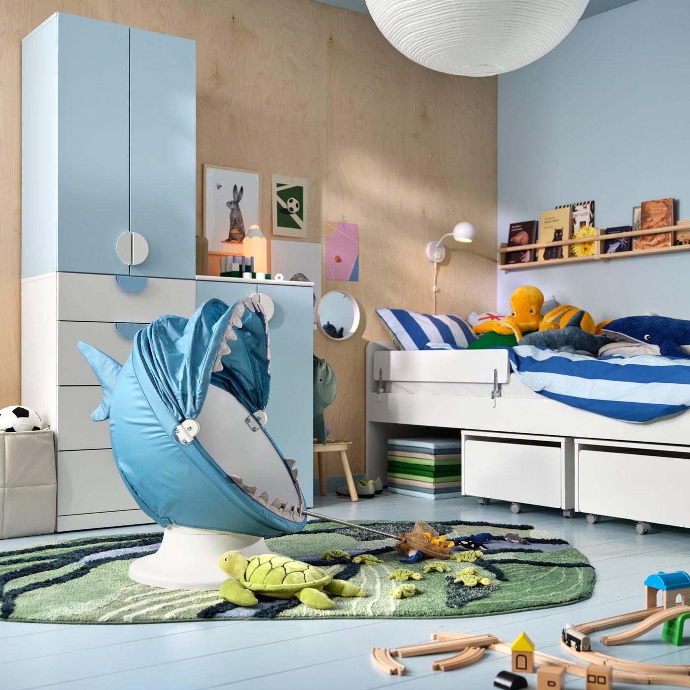 Une chambre d’enfant avec un fauteuil pivotant IKEA PS LÖMSK doté d’une housse représentant un requin, des rangements LASTARE, un lit SLÄKT/NATTAPA et des rangements TROFAST.