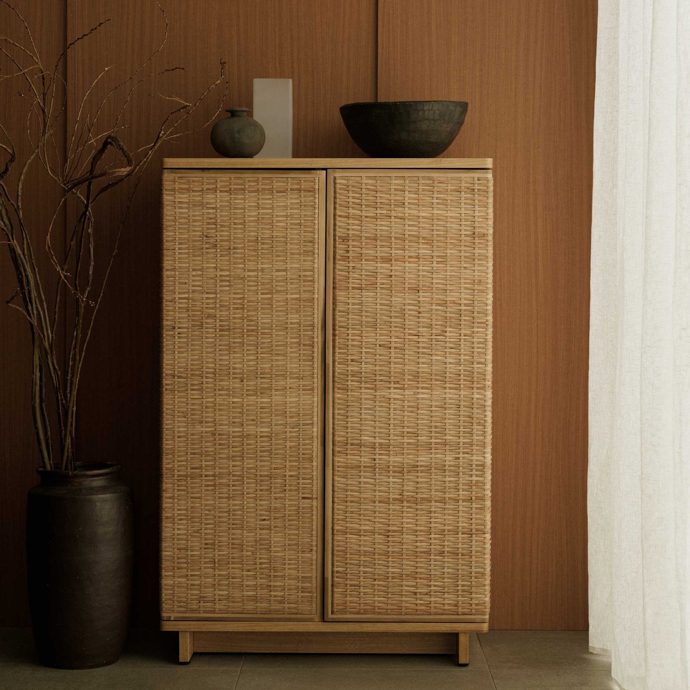 Een Japandi woonkamer met een rotan FRYKSÅS kast tegen een bruine muur aan.