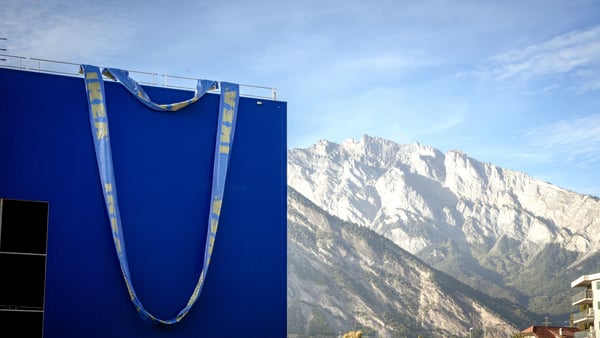 Grande borsa IKEA blu davanti a un paesaggio alpino con cime rocciose e cielo limpido.