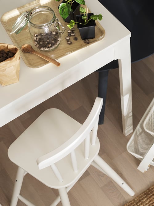 Kitchen with white junior chair, white extendable table, tray, jar with lid, wooden spoon, and blue chair.