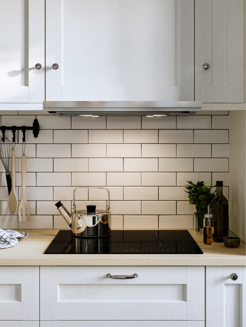 A modern kitchen with a MATMÄSSIG induction hob, white cabinets with doors, a kettle, a spoon and built-in extractor hood.