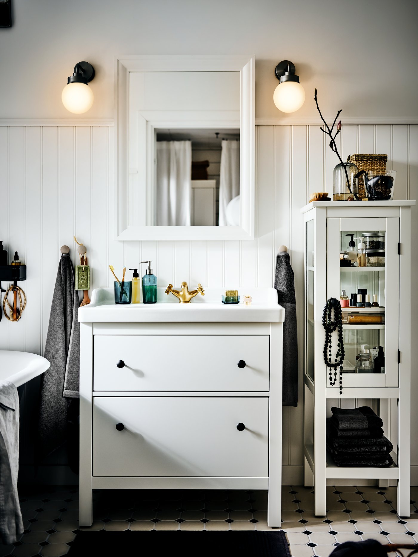 حامل حوض بدرجين HEMNES/RÄTTIVIKEN في حمام مشمس يغلب عليه اللون الأبيض على الطراز الريفي، تعلوه مرآة ومصابيح حائط.