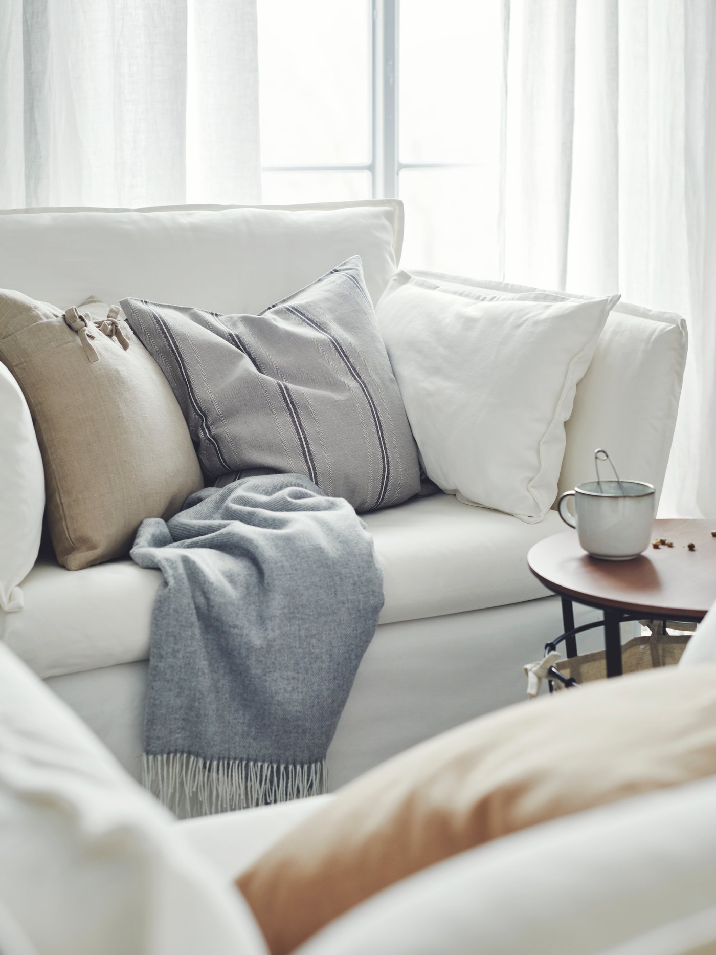Un sofá BACKSÄLEN blanco con muchos cojines y una manta encima.