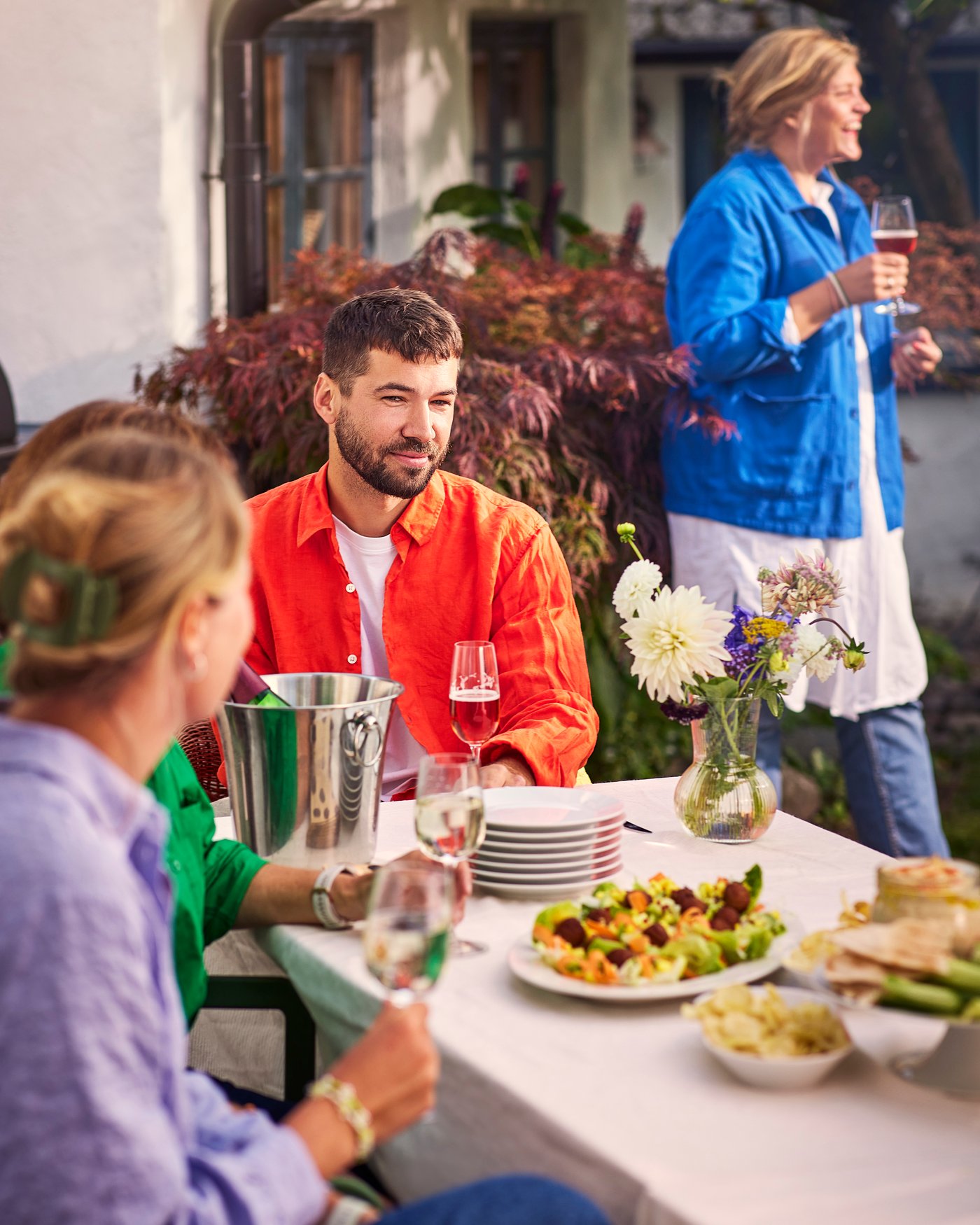 Tre personer sidder ved et vord  dækket op til fest uden for