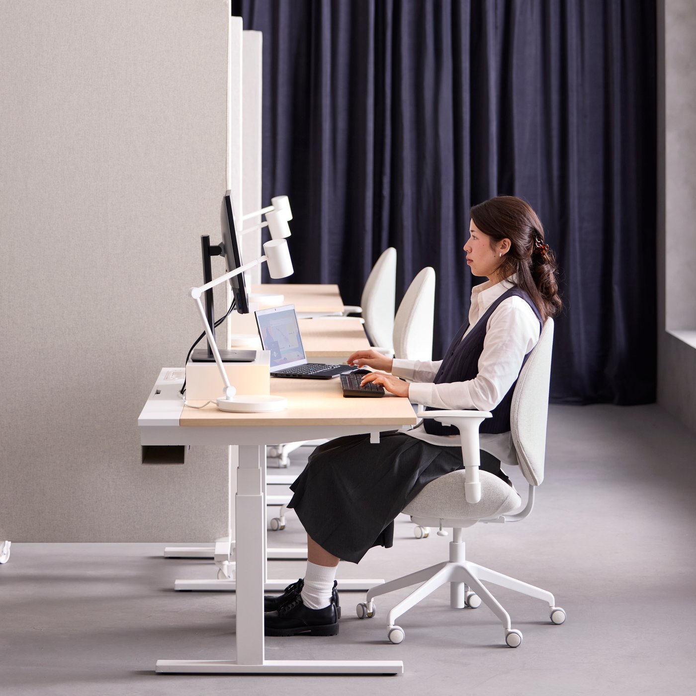 Bureau avec une personne assise utilisant un ordinateur à un bureau assis/debout MITTZON plaqué bouleau/blanc en position basse.