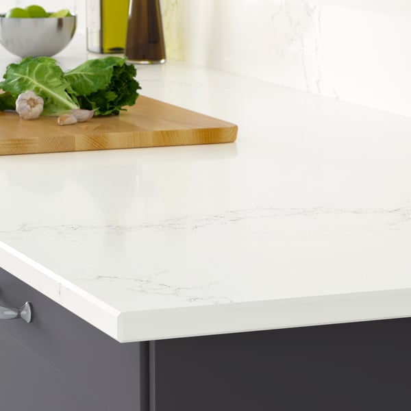 The corner of a LOCKEBO white lively marble effect countertop on a white kitchen cabinet with a stainless steel pot on a trivet.