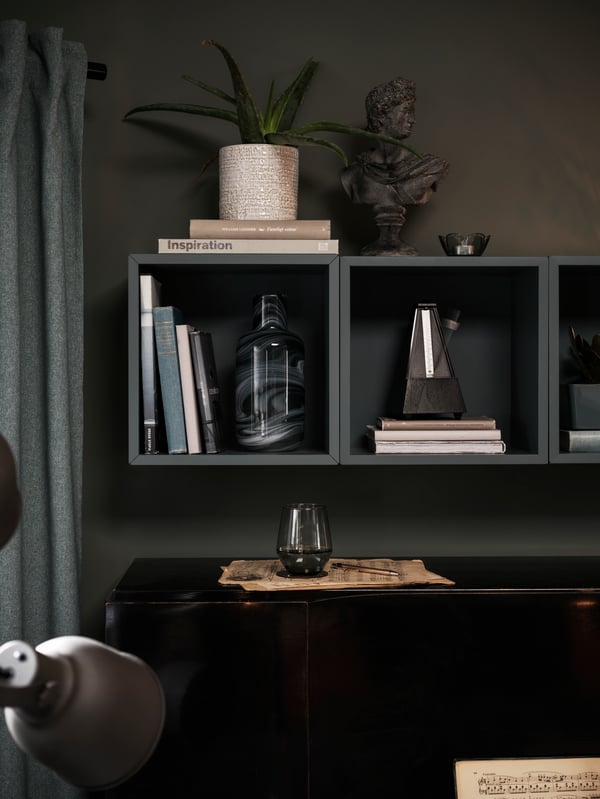 A plant pot and other decorations stand on, and in, a row of grey-turquoise wall-mounted EKET cabinets above a piano.