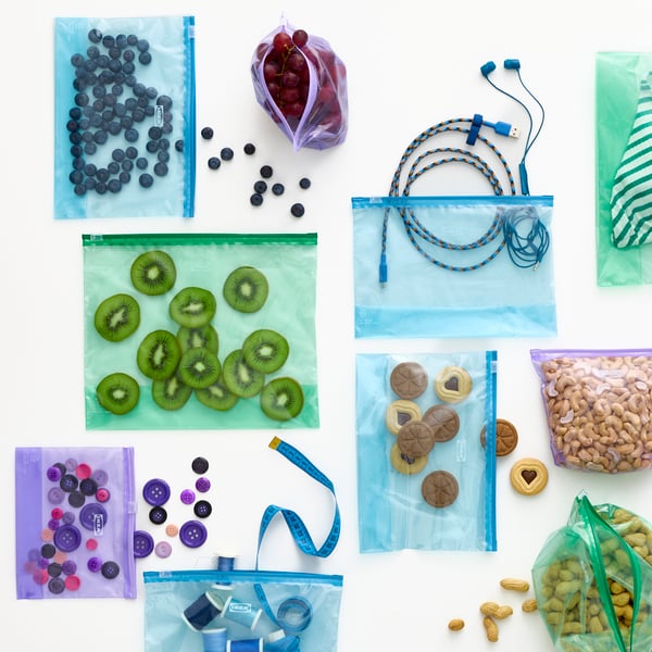A close-up of colourful ISTAD resealable bags filled with snacks, charging cables and crafts arranged on a white surface.