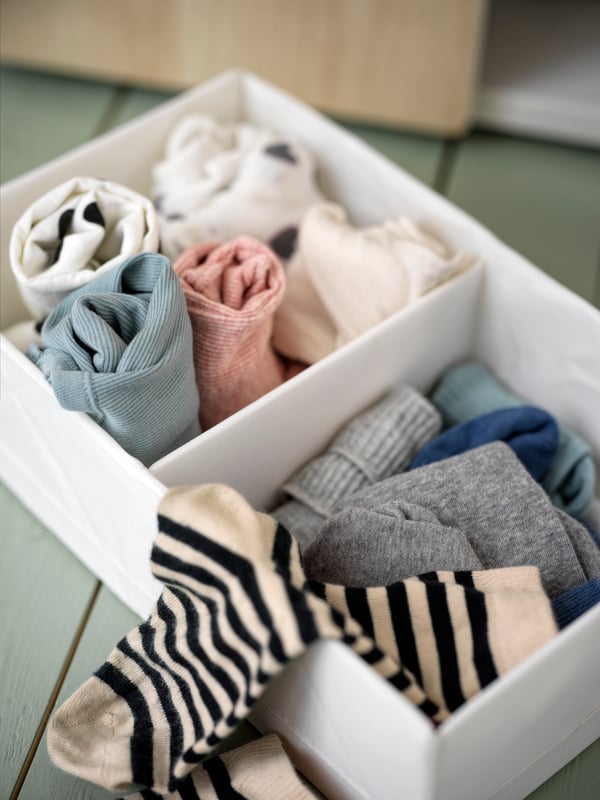 A white STUK storage box with two compartments containing colourful socks and clothes.