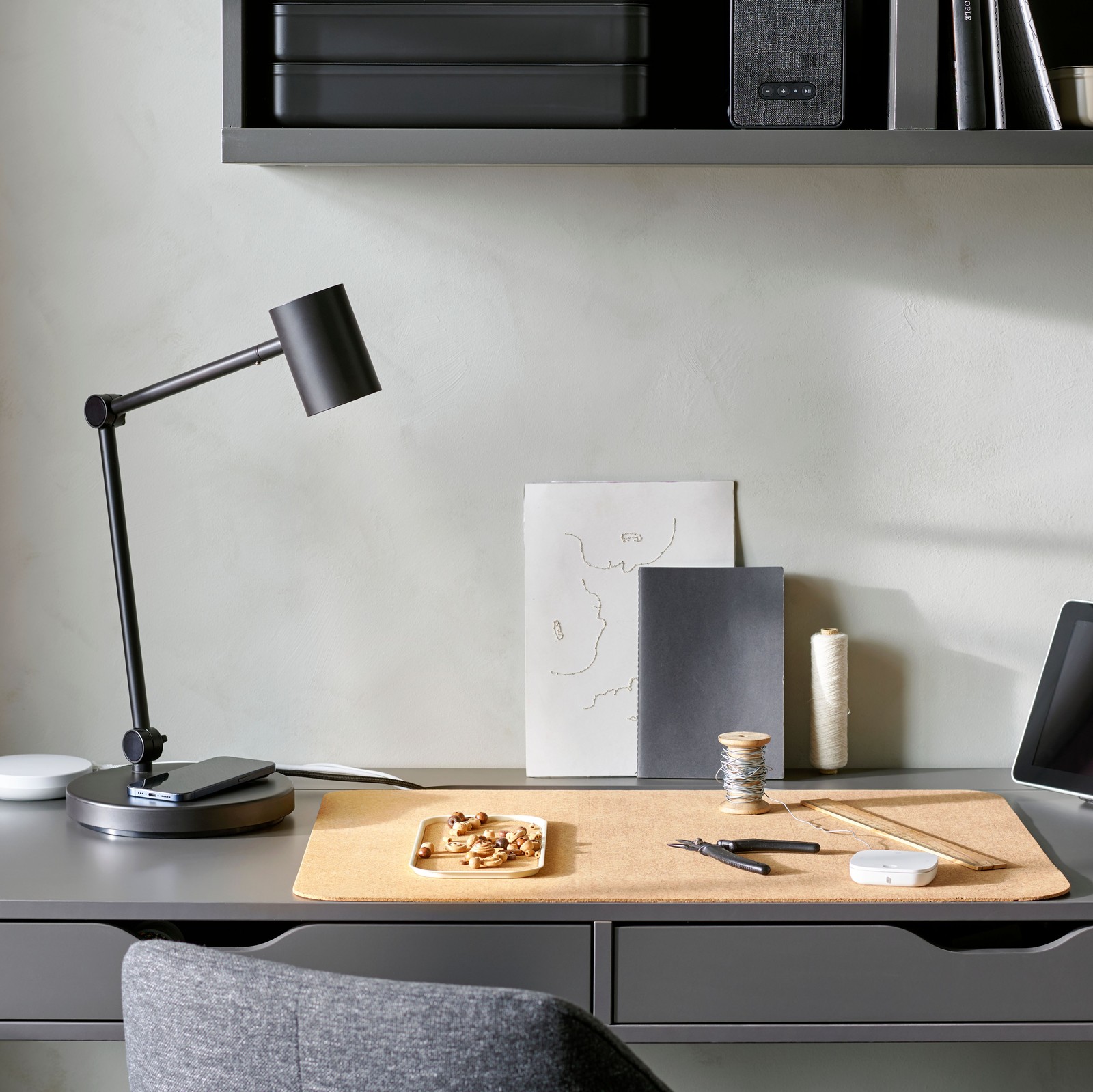 Pe un birou gri se află diverse produse inteligente pentru biroul de acasă, cum ar fi un hub pentru produse inteligente DIRIGERA, o telecomandă și o veioză cu funcție de încărcare încorporată.