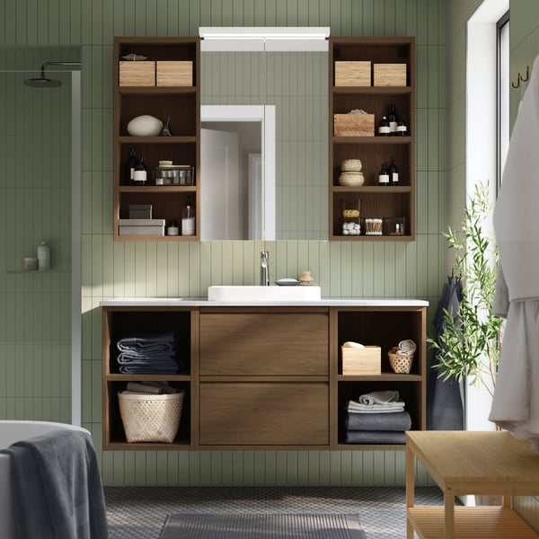 Szafka pod umywalkę ÄNGSJÖN z szufladami zamontowana pod szafką z lustrem w łazience z beżowymi ścianami, częściowo wyłożonymi białymi płytkami ceramicznymi.