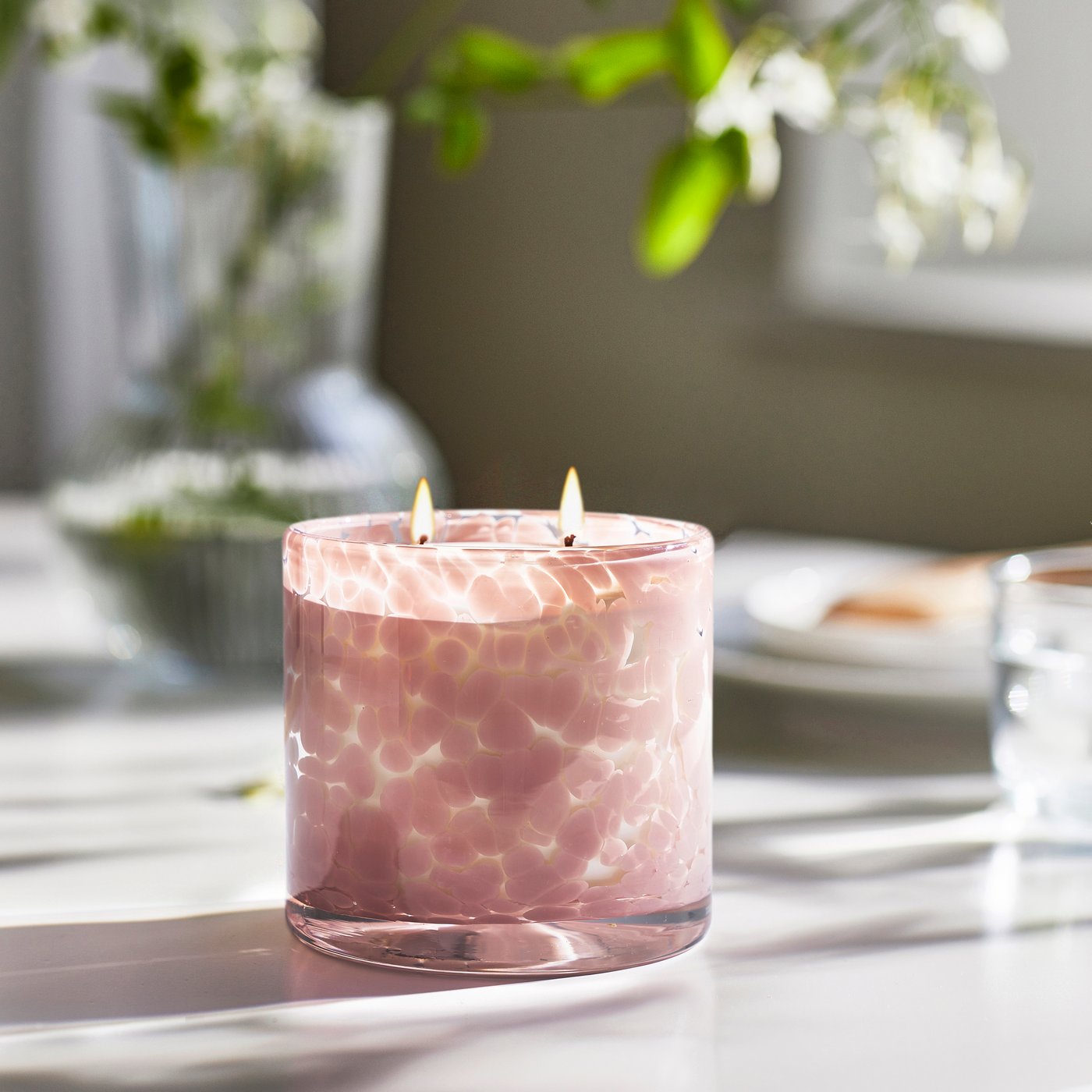 Una candela profumata LUGNARE in vetro rosa chiaro al gelsomino, con due stoppini, che crea un’atmosfera rilassante.