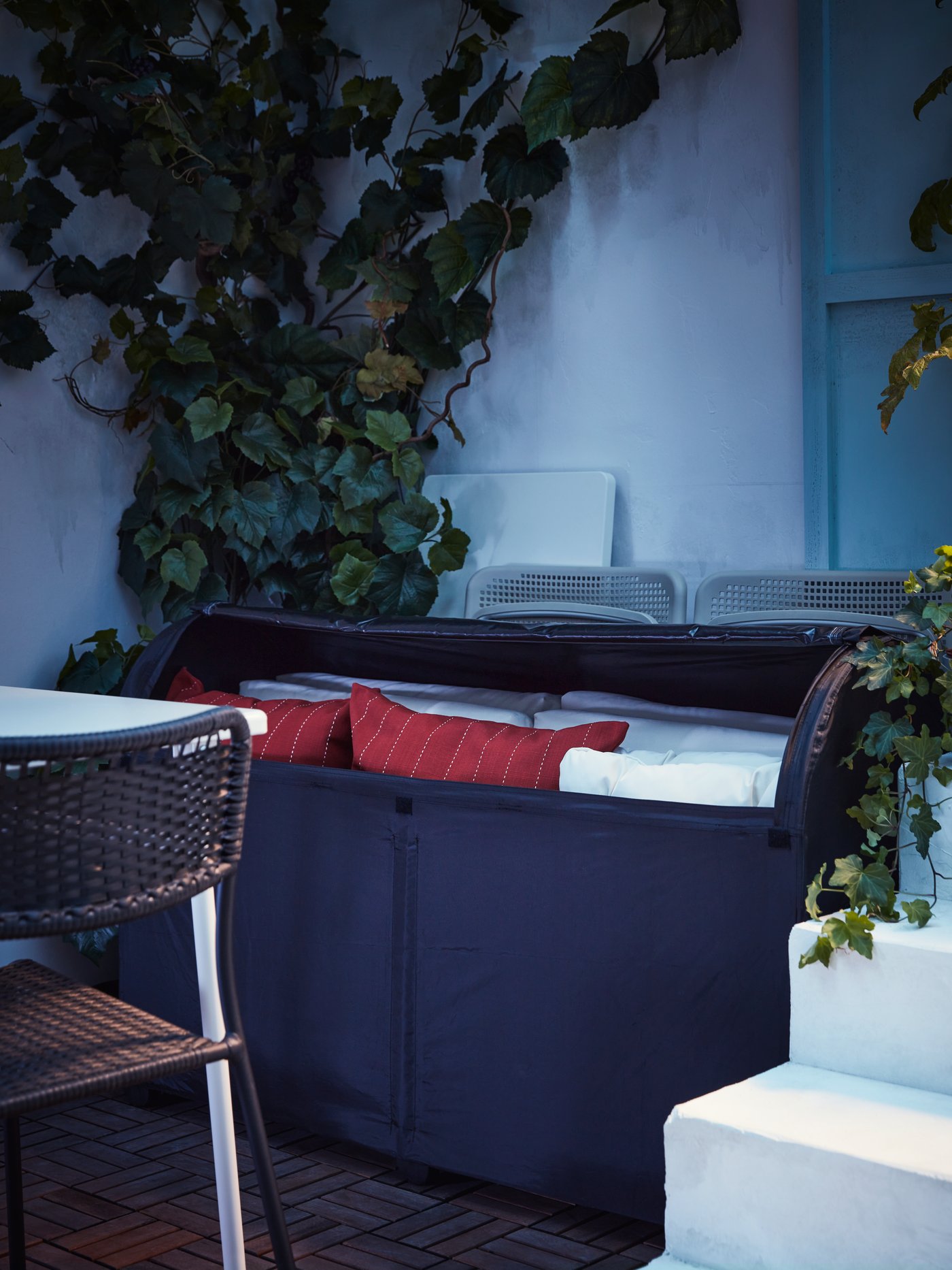 Una caja de almacenamiento TOSTERÖ con cojines de terraza en el interior al costado de un comedor de terraza.