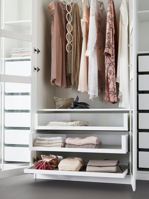Part of a PAX wardrobe with white Tyssedal glass doors has stacked clothes in glass-front drawers below dressers on a rail.