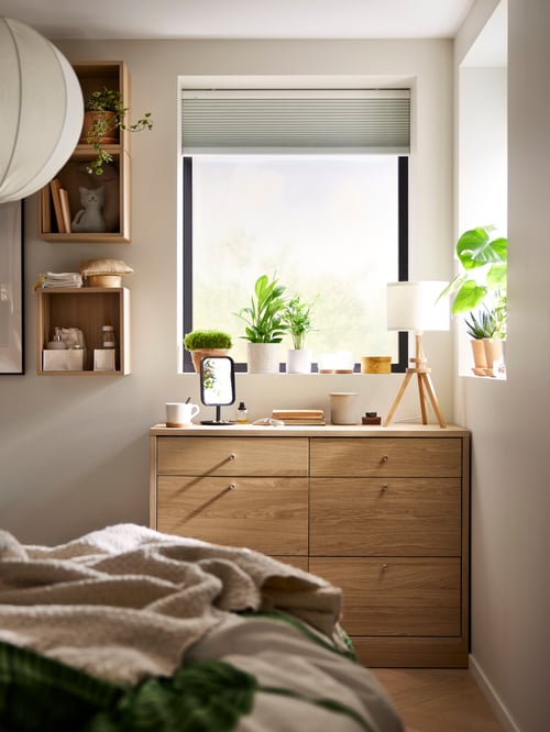 Bedroom corner featuring a TONSTAD chest of 6 drawers made of particleboard, supporting a beige LAUTERS table lamp.