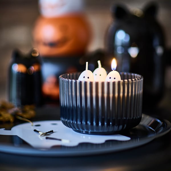 A KUSTFYR glass scented candle, shaped like three ghosts, sits on a KUSTFYR tray with a ghost design.