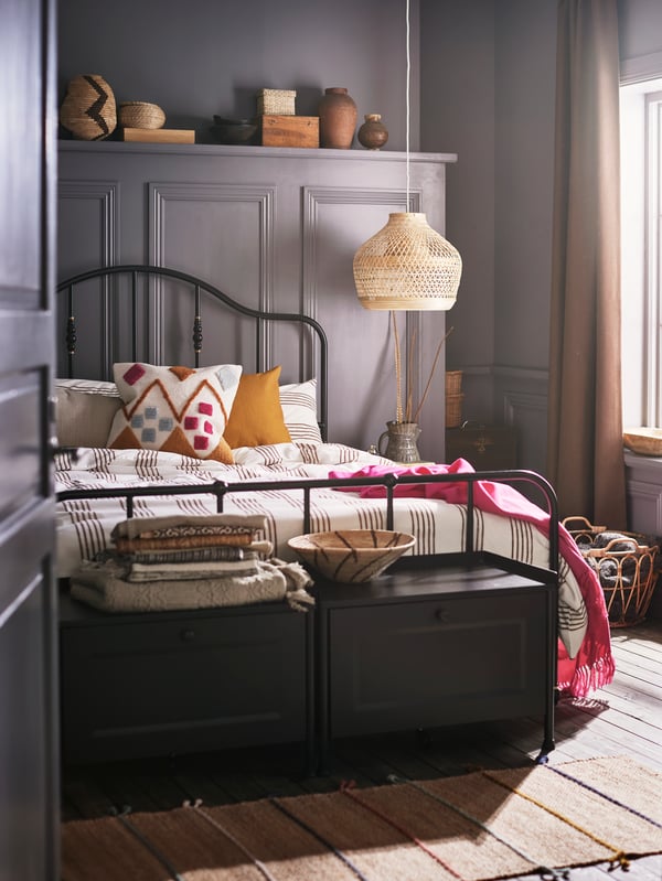 Two black storage benches and a bed with a black bed frame made with striped bed linen and a BRUNSTARR multicolour cushion.