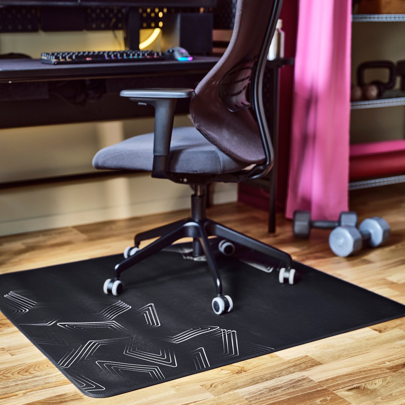 Una silla gamer UTKLASSNING en antracita y negro colocada sobre un protector de piso LÅNESPELARE negro con un patrón gráfico blanco.