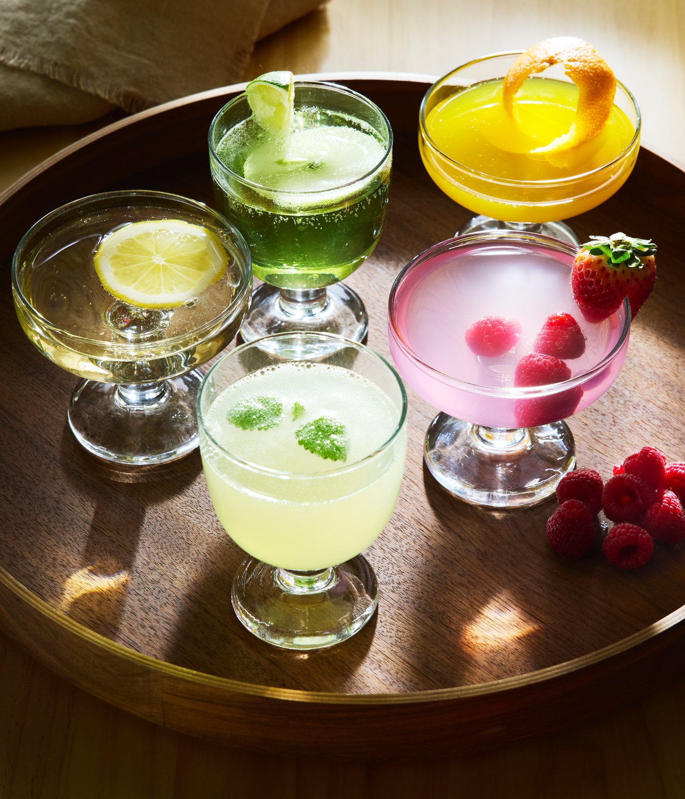 Two FRUKTDUVA goblets and three FRUKTDUVA champagne coupes filled with various drinks stand on an OMBONAD tray.